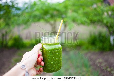woman's hand holding a jar with green cold-pressed juice, nature background. Healthy eating, detoxing, juicing, body cleancing concept 