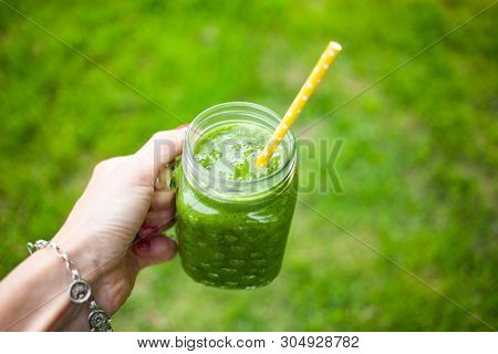 woman's hand holding a jar with green cold-pressed juice, nature background. Healthy eating, detoxing, juicing, body cleancing concept 