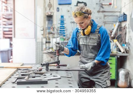 Female mechanic working with clamp and spanner on metal workpiece