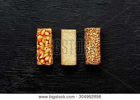 Cereal Granola Bar With Peanuts, Sesame And Sunflower Seeds On A Cutting Board On A Dark Stone Table