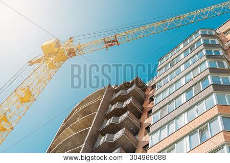 Building Under Construction And Construction Crane Against Blue Sky And Bright Sun On Summer Day. Bo