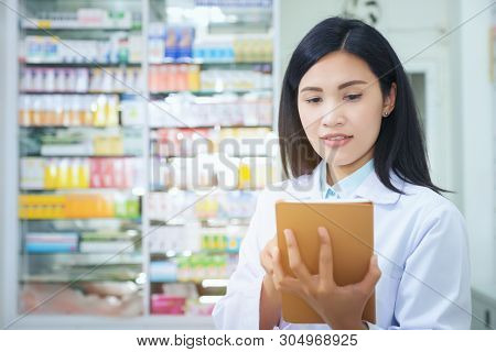 Pharmacist Working With A Tablet Computer In The Pharmacy Holding It In Her Hand While Reading Infor