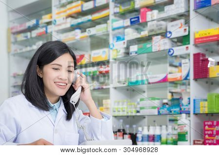 Pharmacy Worker Talking By Phone, Attractive Young Smiling Female At Desk With Telephone To Ear