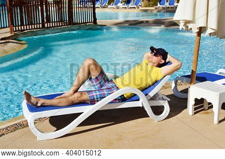 Young And Successful Man Lying On A Sun Lounger At The Hotel Near Sweeming Pool. Relax In Summer Poo