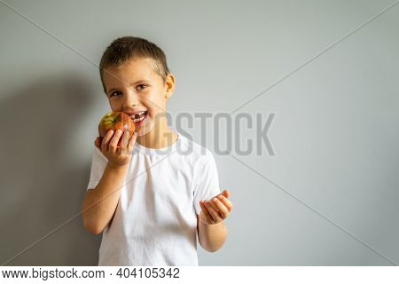 Boy Without Milk Upper Tooth In White T-shirt Holds An Apple In Hand On The Gray Background.