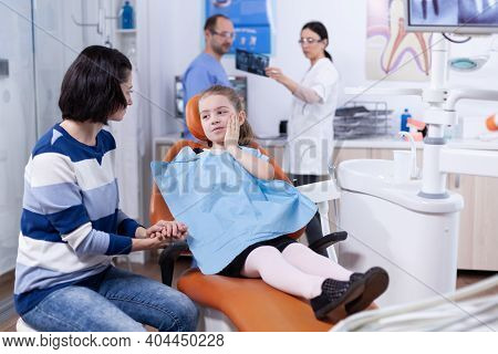 Little Girl In Dentist Office Showing Parent Where Tooth Hurts Touching Face With Painfull Expressio
