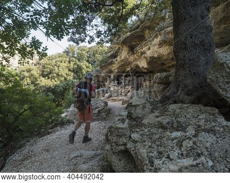 Man Hiker At Rocky Hiking Path To Cala Goloritze Beach With Limestone Rocks, Trees And Green Bush. F
