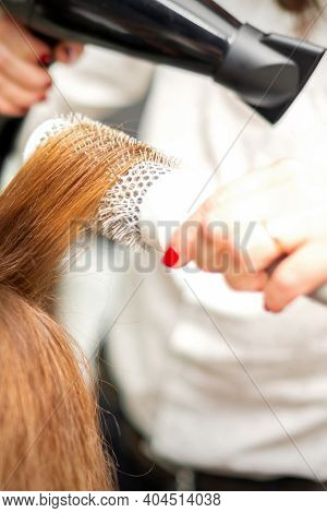 Close Up Of Hairdresser Drying Long Red Hair With A Hairdryer And Round Brush In A Beauty Salon