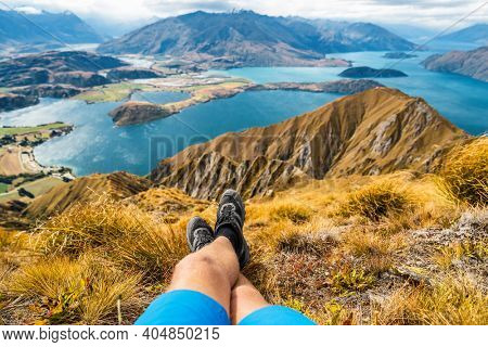Adventure and hiking wanderlust travel vacation concept with hikers hiking boots close up. Hiker man looking at view from famous hike to Roys Peak on South Island, New Zealand. Resting and relaxing.