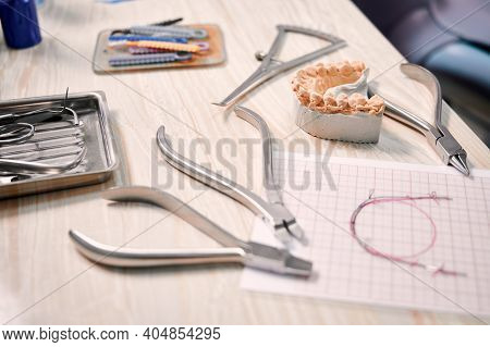 Desk With Orthodontic Tools, Ligature Ties, Dental Teeth Model And Wire Braces Drawing. Ligature Wir