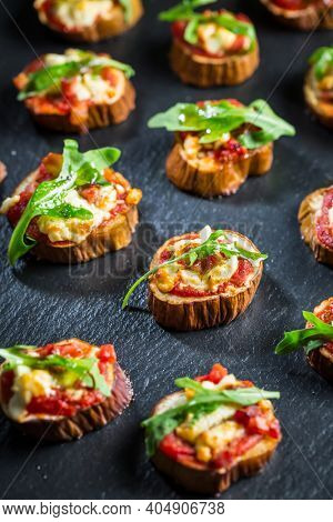 Mini eggplant appetizers with tomato, cheese and salad on black background. Healthy pizza snack