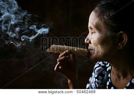 Old wrinkled Asian woman smoking traditional tobacco. Bagan, Myanmar.
