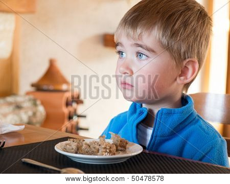 Grievous little boy sitting behind table with full plate