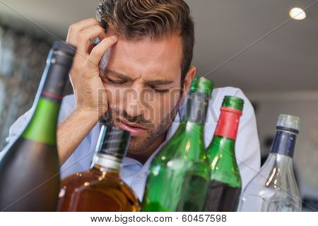 Drunk businessman slumped beside many spirit bottles at the local bar