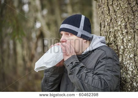 Worried man breathe into a paper bag near tree