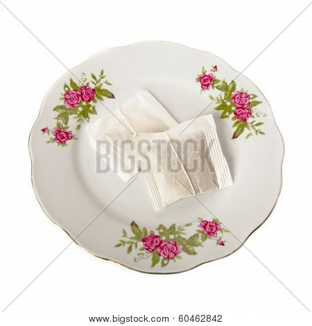 Two bags of tea on a white porcelain plate with floral ornament isolated over white