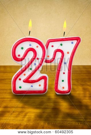 Burning birthday candles number 27 on a wooden background
