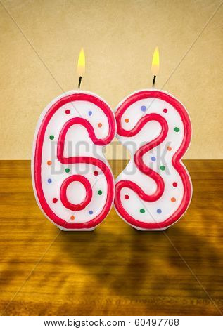 Burning birthday candles number 63 on a wooden background
