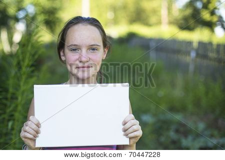 Teengirl, outdoors, holding clean white sheet paper, banner for your message.