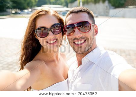 love, wedding, summer, dating and people concept - smiling couple wearing sunglasses making selfie in city