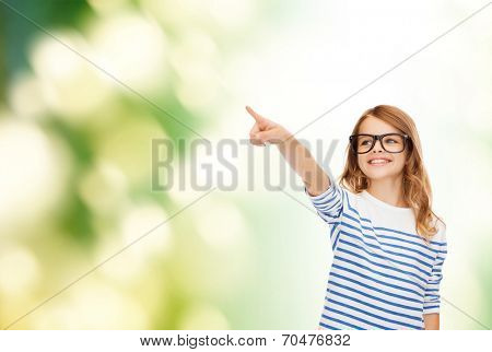 education, school and imaginary screen concept - cute little girl in eyeglasses pointing in the air or imaginary screen