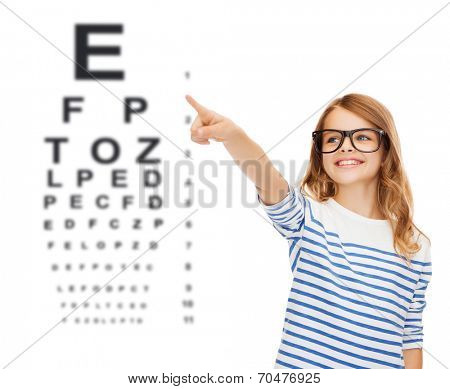 education, school and imaginary screen concept - cute little girl in eyeglasses pointing in the air or imaginary screen