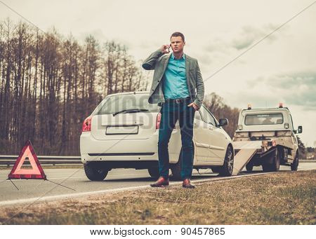Man calling while tow truck picking up his broken car 