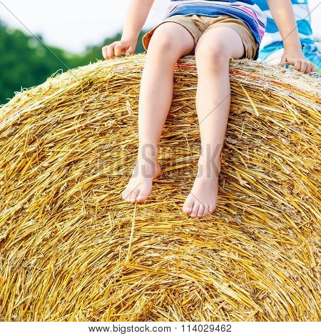 Little kid boy sitting on hay bale in summer