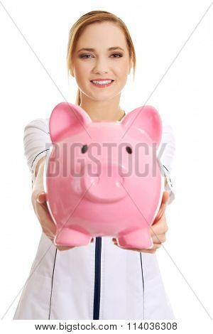 Young female doctor holding a piggybank.