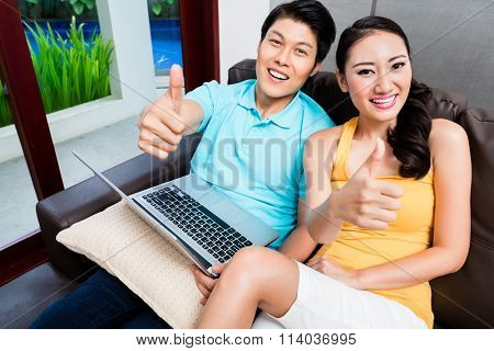 Asian woman and man surfing showing thumbs up in their living room at home