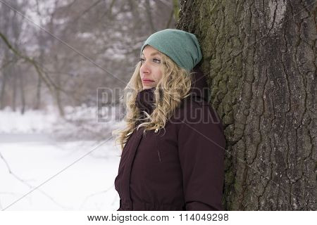 sad woman leaning against tree in winter