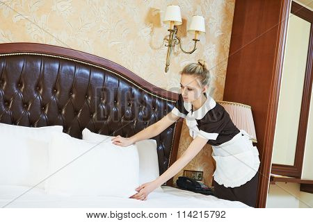 Hotel service. female housekeeping worker maid making bed with bedclothes at inn room