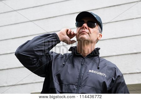 Confident Security Guard Listening To Earpiece Against Building