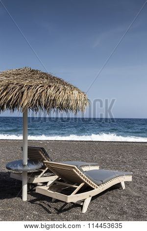 View Of Perissa Beach On The Greek Island Of Santorini With Sunbeds And Umbrellas. Beach Is Covered