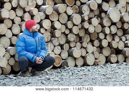 Hunkering worker having a rest at pile of logged firewood background outdoors in winter mountain for