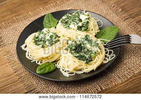 Italian pasta with spinach and feta on black plate on the wooden background.