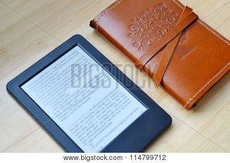 Black ereader with reading glasses and an old notebook in leather cover on wooden table