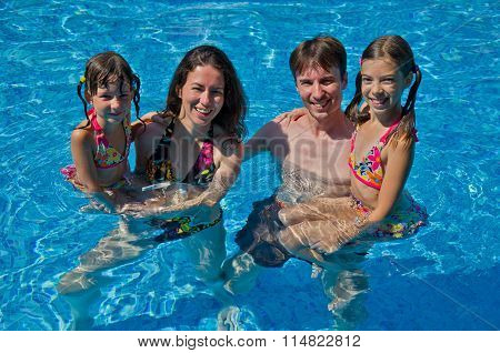 Happy family with two kids in swimming pool. Smiling parents and children on summer vacation