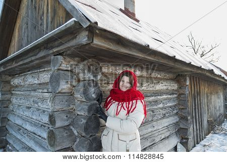 The Russian woman in  shawl warms hands near an izba