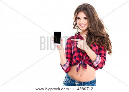 Happy beautiful young woman with long curly hair holding blank screen mobile phone and pointing on it over white background