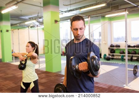 sport, fitness, lifestyle and people concept - woman with kettlebell and man with dumbbell exercising in gym