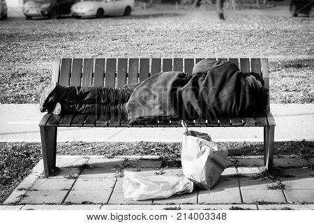 Homeless refugee man in black coat sleeps on the bench on the street black and white