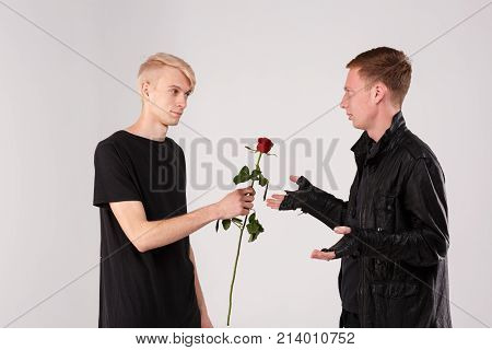 Two young guys are brunette and blond. A guy with blonde hair gives a brunette guy a rose to a who is indignant. Isolation.