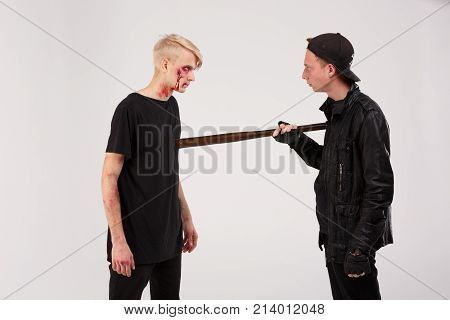 A dangerous guy in a cap and a wooden bit in his hands is threatening a battered boy. Isolation.