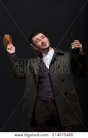 A man on a black background, retro style, holds in his hand a bottle of alcohol, in the second hand a brown cap, which he tries to throw away.