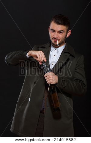 A man on a black background, retro style, smiles, opens a bottle of alcohol with a corkscrew, a cigarette sticks out in his mouth.