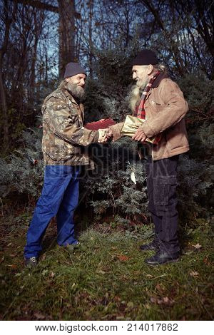 Two homeless older men celebrating christmas in park with gifts