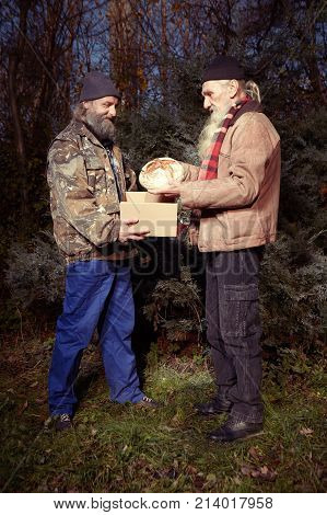 Two homeless older men celebrating christmas in park with gifts of food