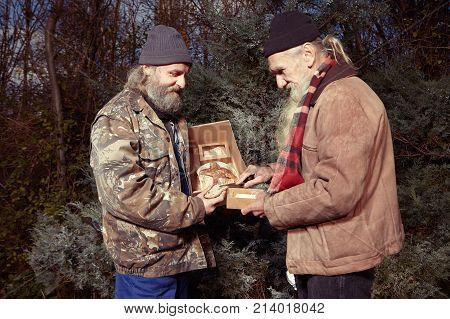Two homeless older men celebrating christmas in park with gifts of food