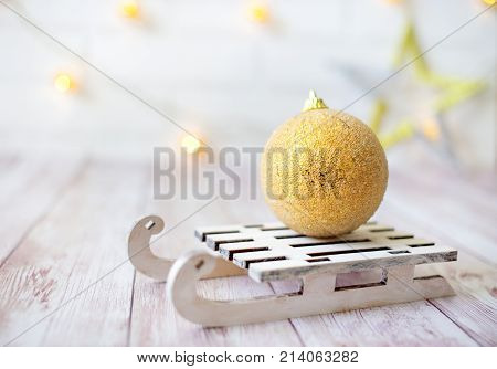 Shining Christmas Ball On Toy Wooden Sled On Light Bokeh Background With Goolden Star. New Year Card